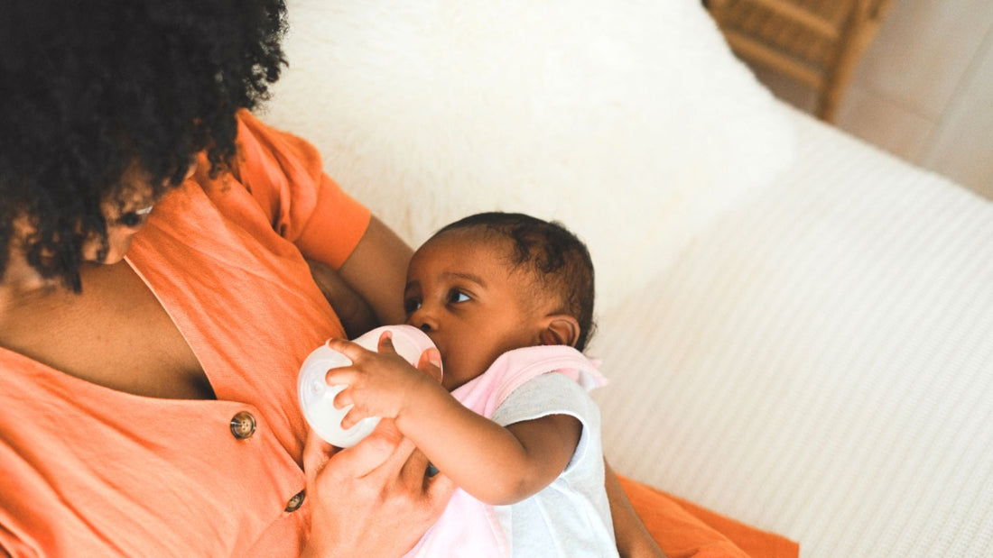 mama feeding newborn baby with baby bottle on sofa