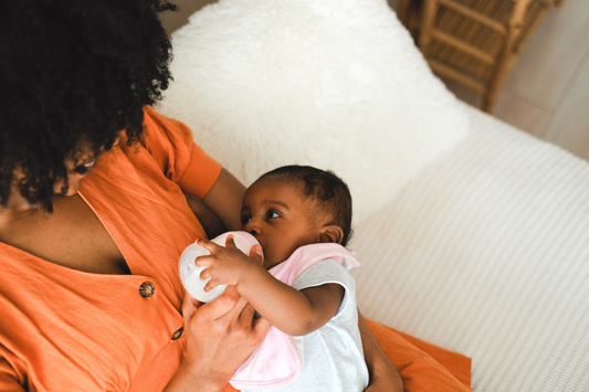 mama feeding newborn baby with baby bottle on sofa