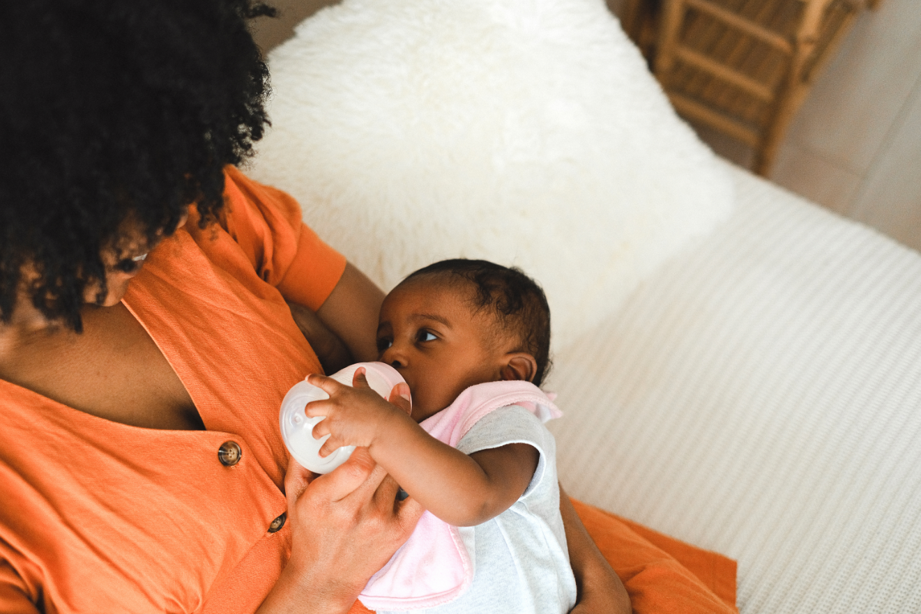 mother feeding baby milk in bottle on sofa