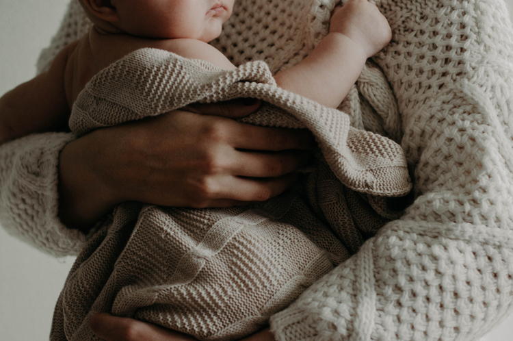 baby wrapped in blanket getting cuddle from mother in jumper